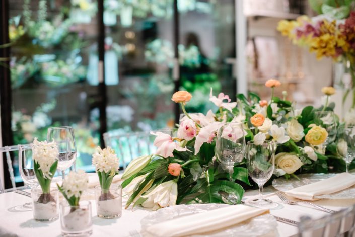 Hyacinth flowers in clear glass vases with floral arrangement in peach ranunculus and white flowers with monstera leaves and clear glass chiavari chairs