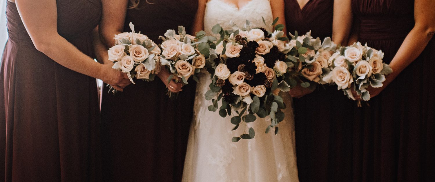 Bride with bridal bouquet of blush roses, burgundy dahlia and eucalytpus and bridesmaids in burgundy with quicksand rose bouquets