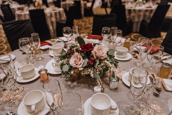 Wedding tablecenter designed with burgundy dahlia, blush roses, pieris japonica and snowberry