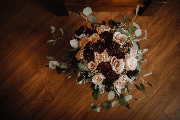 Top view of bridal bouquet designed with burgundy dahlia, blush roses, scabiosa pods, and ivory garden roses with silver dollar eucalyptus