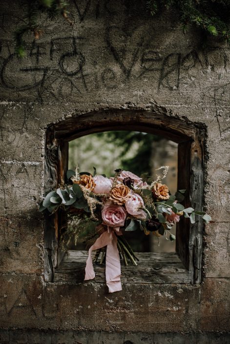 bridal bouquet sitting in concrete wall window designed with pink ohara garden roses, toffee roses and gold plumosa and cinerea eucalyptus with blush silk ribbon tie