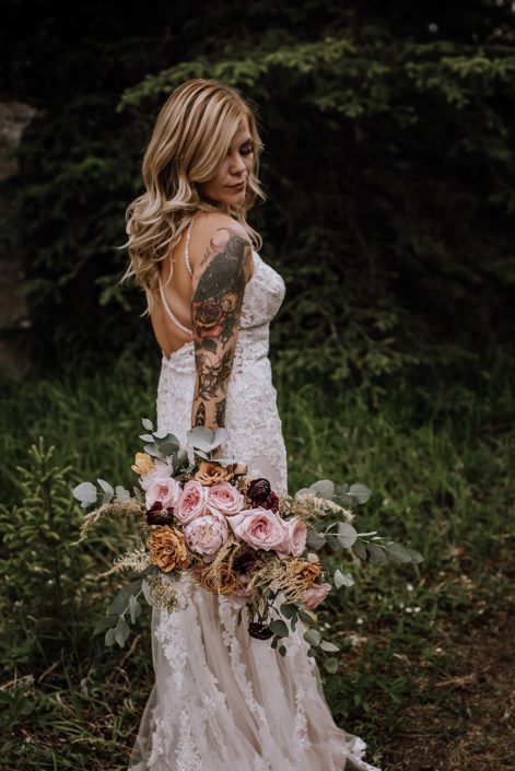 Tattoo sleeve bride in white lace wedding dress holding organic bridal bouquet of pink o'hara roses, toffee roses, cinerea eucalyptus and gold plumosa