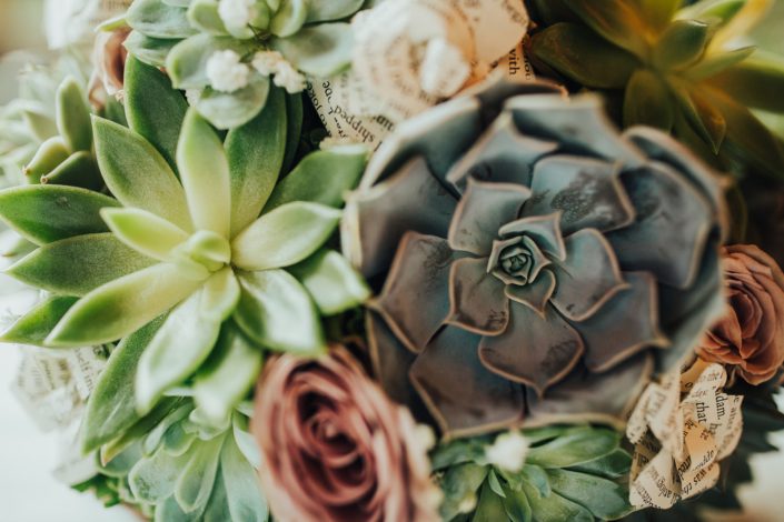 Close up photo of succulent bridal bouquet with tucks of mauve amnesia roses and book paper flowers