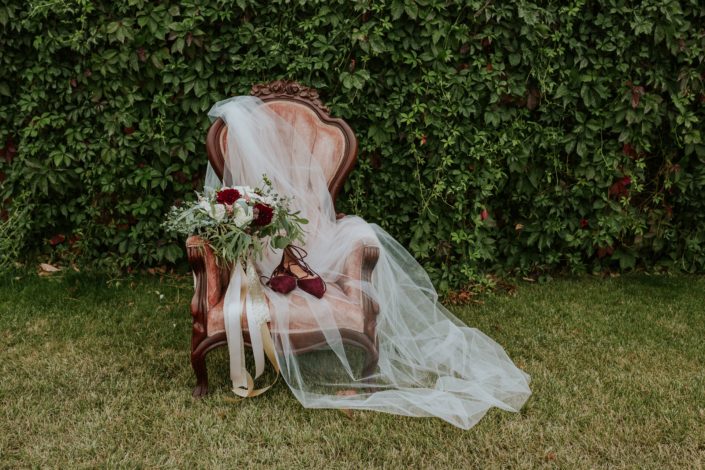 Antique dusty rose chair with bride;s cathedral veil, burgundy shoes and burgundy dahlia, quicksand rose and ivory rose bridal bouquet