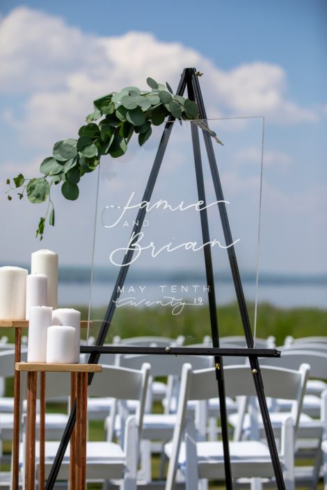 clear acrylic wedding welcome sign on black easel with white pillar candles and fresh eucalyptus greenery accent