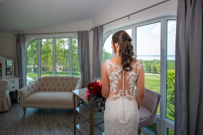Hilltop wedding venue brida suite with bride in lace wedding dress with button down back and holding a bridal bouquet of burgundy peony and black monstera leaves