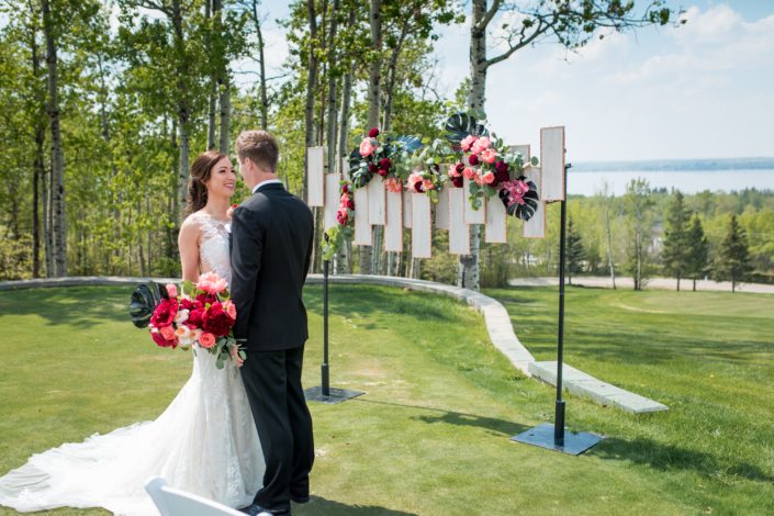 bride and groom with coral and burgundy bridal bouquet and archway geometric backdrop in coral peonies and black monstera