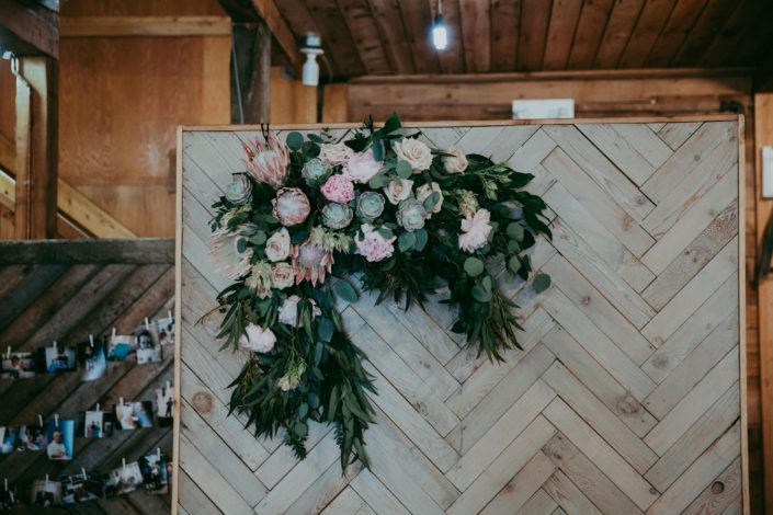 Rustic barnwood backdrop with fresh flower arrangement of king protea, eucalyptus, succulents, peonies and roses