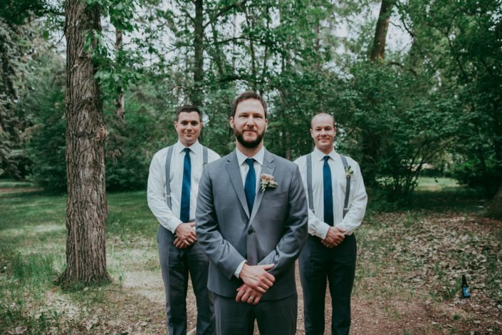 Groom in charcoal suit with navy tie wearing succulent boutonniere with groomsmen in charcoal pants and suspenders with navy ties