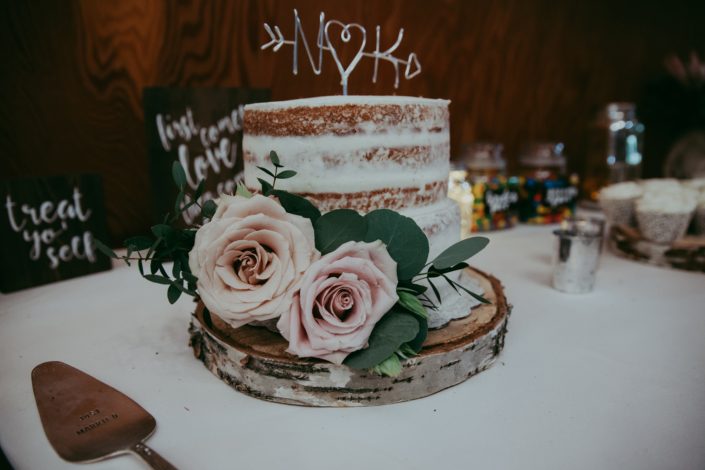 Rustic naked cake on birch wood cookie with N and K monogram and accent of eucalyptus and quicksand roses