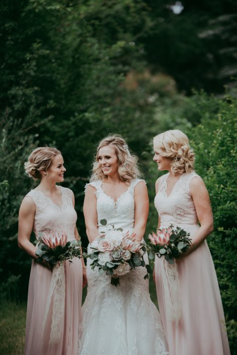 Blond bride with bridesmaids holding bridal bouquet of white peony, succulent, blush rose and pale pink king protea and silver dollar eucalyptus and bridesmaids in blush with pale pink king protea