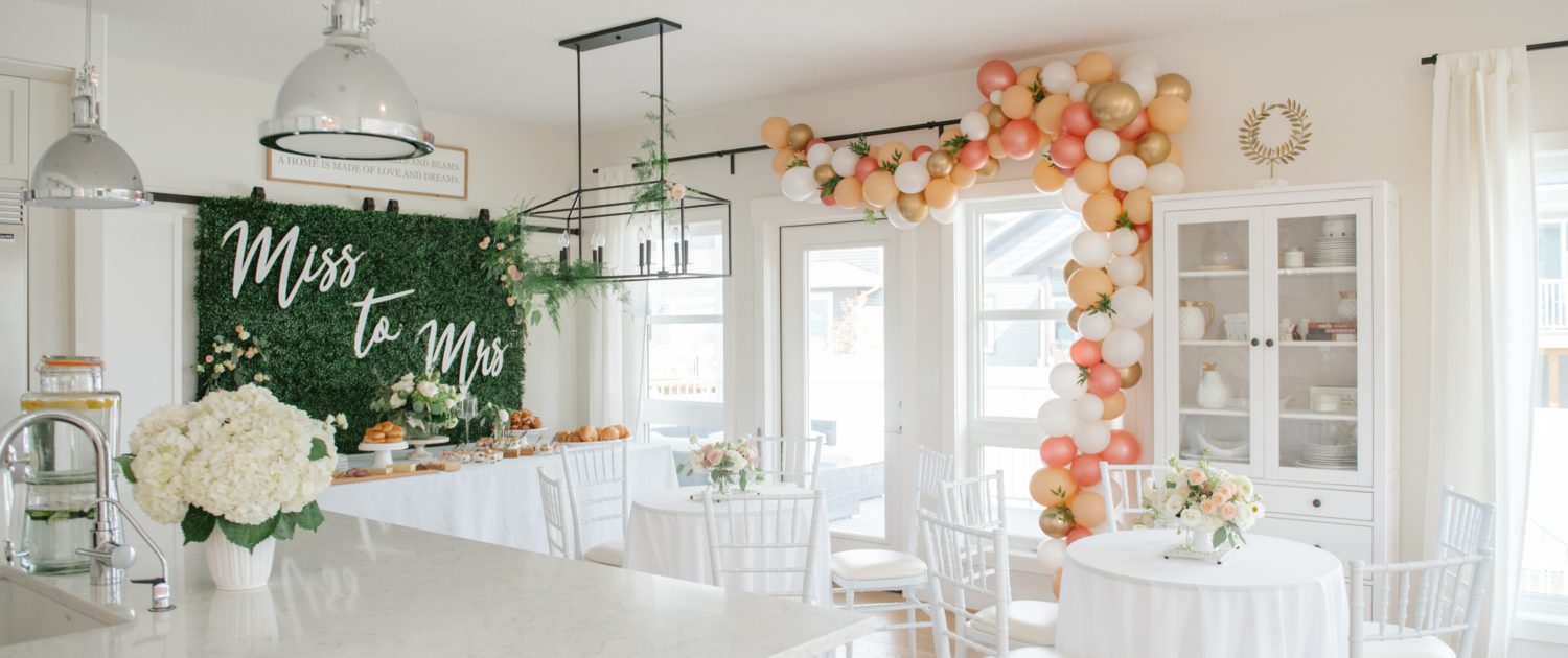 Bridal shower in white house with ocktail table arrangements and boxwood backdrop and balloon garland in blush, peach and gold with hydrangea flower arrangements