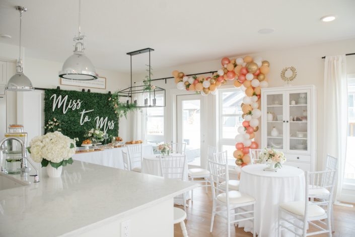 Bridal shower in white house with ocktail table arrangements and boxwood backdrop and balloon garland in blush, peach and gold with hydrangea flower arrangements