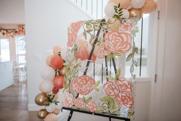 Bridal shower welcome sign with balloon garland and accents of italian ruscus in gold, peach and blush
