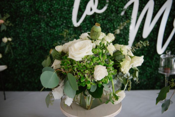 Floral arrangement with boxwood backdrop designed in a clear glass vase with green hydrangea, white roses and white ranunculus