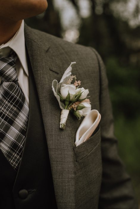 groom in charcoal grey suit with boutonniere of white spray roses and pale pink astilbe and dusty miller