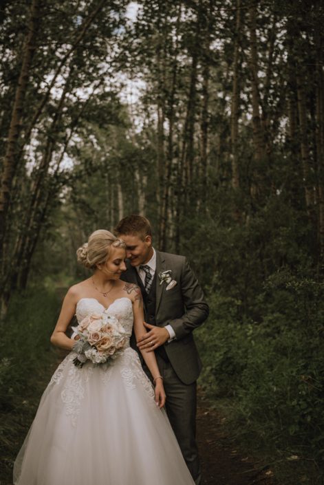 bride in strapless wedding dress with groom in grey suit holding a bridal bouquet of hydrangea, blush roses and dusty miller