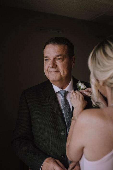 bridesmaid pinning on white rose boutonniere to father