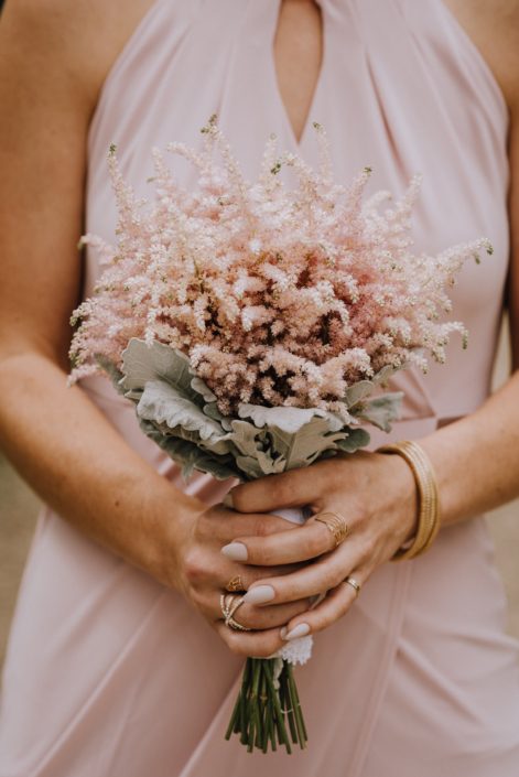 bridesmaid in blush dess holding bouquet of pale pink astilbe with dusty miller collar