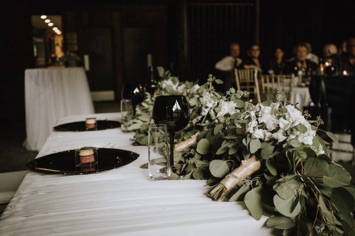 sweetheart table with bridesmaid bouquets and eucalyptus garland and black charger plated and wine glasses