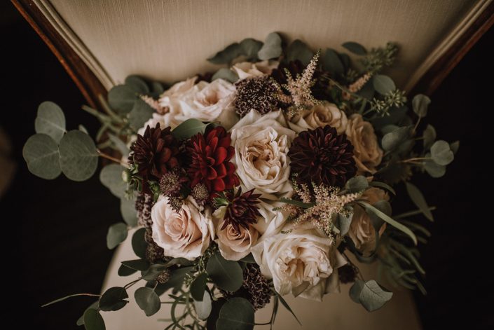 close up of bridal bouquet on antique ivory chair designed with plum scabiosa, burgundy dahlia, white ohara garden roses, quicksand roses, burgundy astrantia and pale pink astilbe