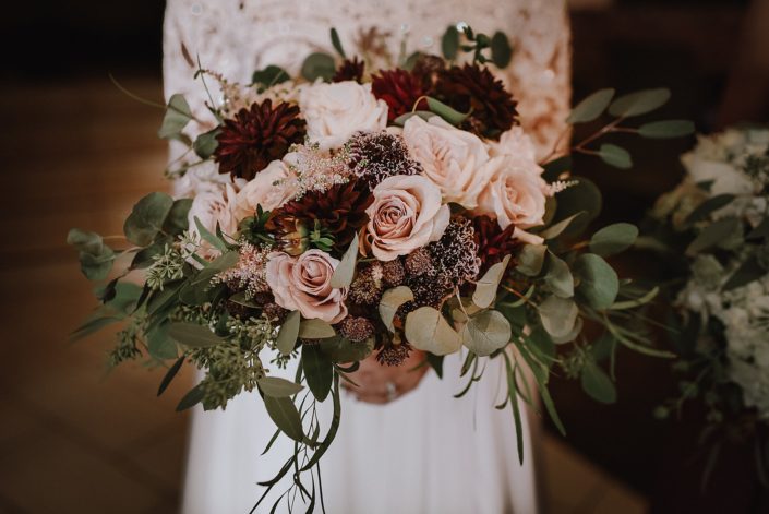 close up of bridal bouquet designed with eucalyptus and burgundy dahlia, blush quicksand roses, plaum scabiosa, burgundy astrantia and pale pink astilbe