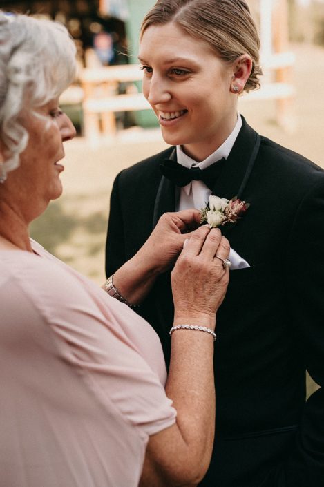 grandmother pinning on boutonniere to bride wearing tuxedo