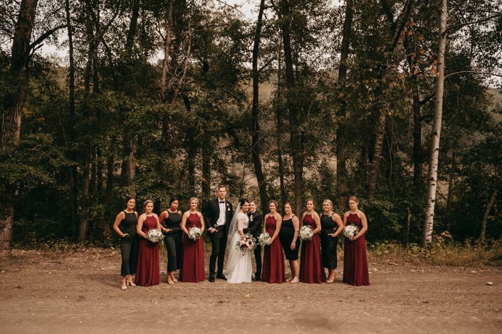 wedding party with bridesmaids in black jumpsuits and burgundy long dresses with white hydrangea bouquets