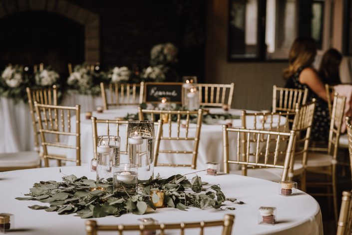 centerpiece at canyon ski resort with white linens, gold chivari chairs and centerpiece of eucalyptus greenery and cylinder vases with candles