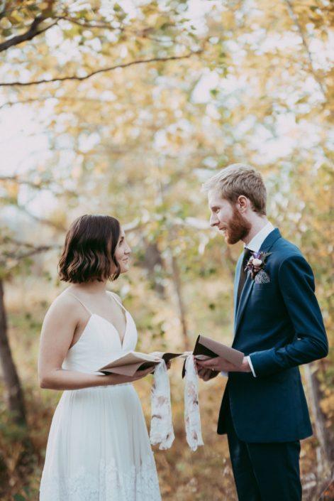 bride and groom with vow books in front of autumn trees
