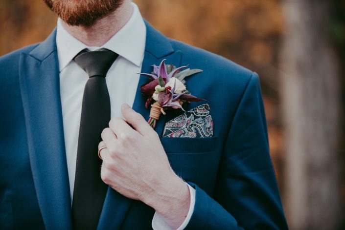 Groom in navt blue suit with paisley pocket square with leather wrapped boutonierre designed with purple clematis and blush spray rose