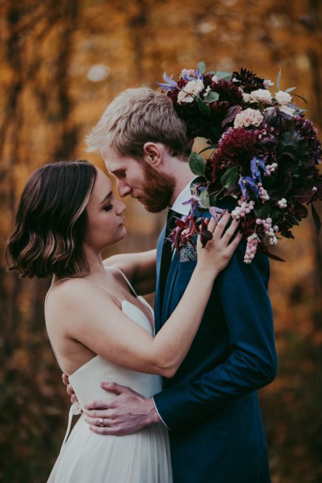 bride in white dress holding a bridal bouquet with burgundy hydrangea and amaranthus ad blush roses and carnations and groom in navy suit with boutonniere