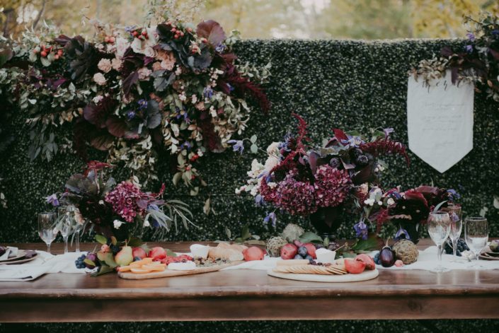 Box wood backdrop with fresh floral accents and menu banner with harvest table and floral designs and charcuterie boards
