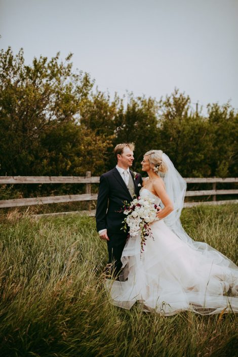 bride and groom in alberta summer wheat field holding a cascade bridal bouquet of white dendrobium orchids and burgundy dendrobium and cymbidium orchids