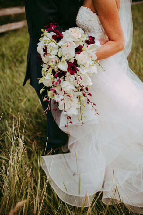 Bride holding a cascade bouquet designed with white cymbidiu orchids and dendrobium orchids and white calla lilies and roses
