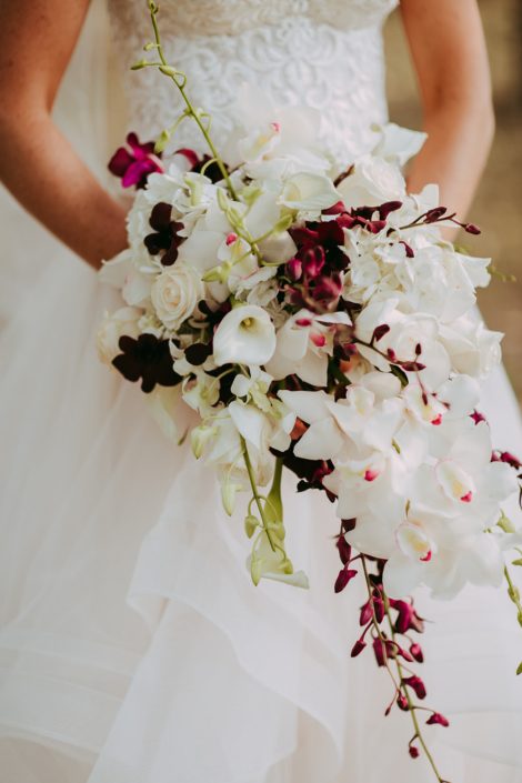 bride holding a cascade bouquet designed with white calla lilies, burgundy orchids and white cymbidium orchids