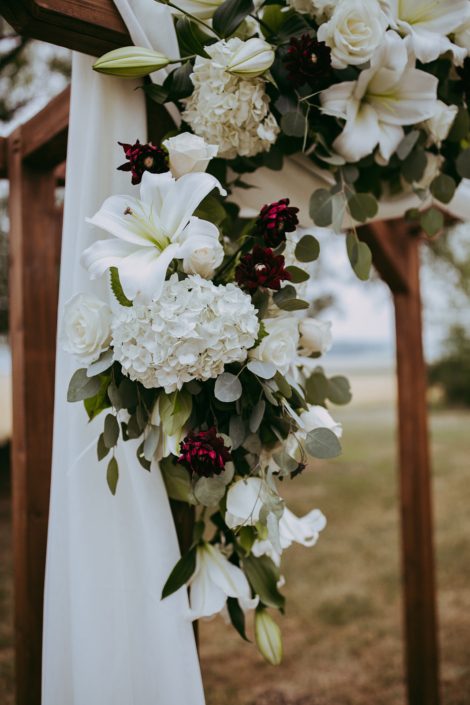 Archway arrangement designed with white lilies and hydrangea and roses and burgundy dahlia with white voile