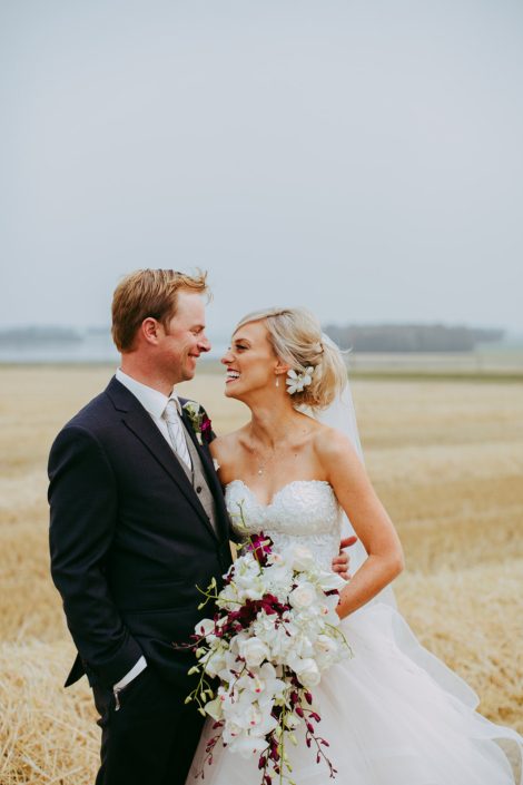 bride and groom in an alberta summer wheat field wedding holding a bridal bouquet designed with white orchids and calla lilies