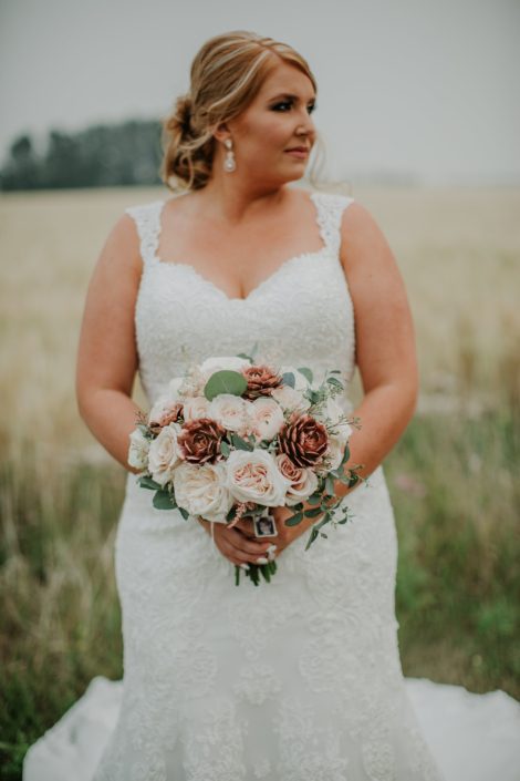 Bride in a late summer wheat field in alberta holding a bridal bouquet designed with rose gold succulents ad white ohara garden roses and blush quicksand roses
