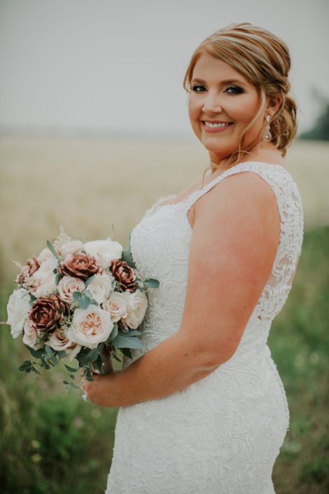 Bride in a summer wheat field with wedding dress and bridal bouquet of rose gold succulents and ivory garden roses and blush roses and eucalyptus