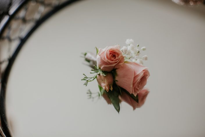 small spray rose boutonniere designd with blush spray roses and white babies breath and eucalytpus in a mirror