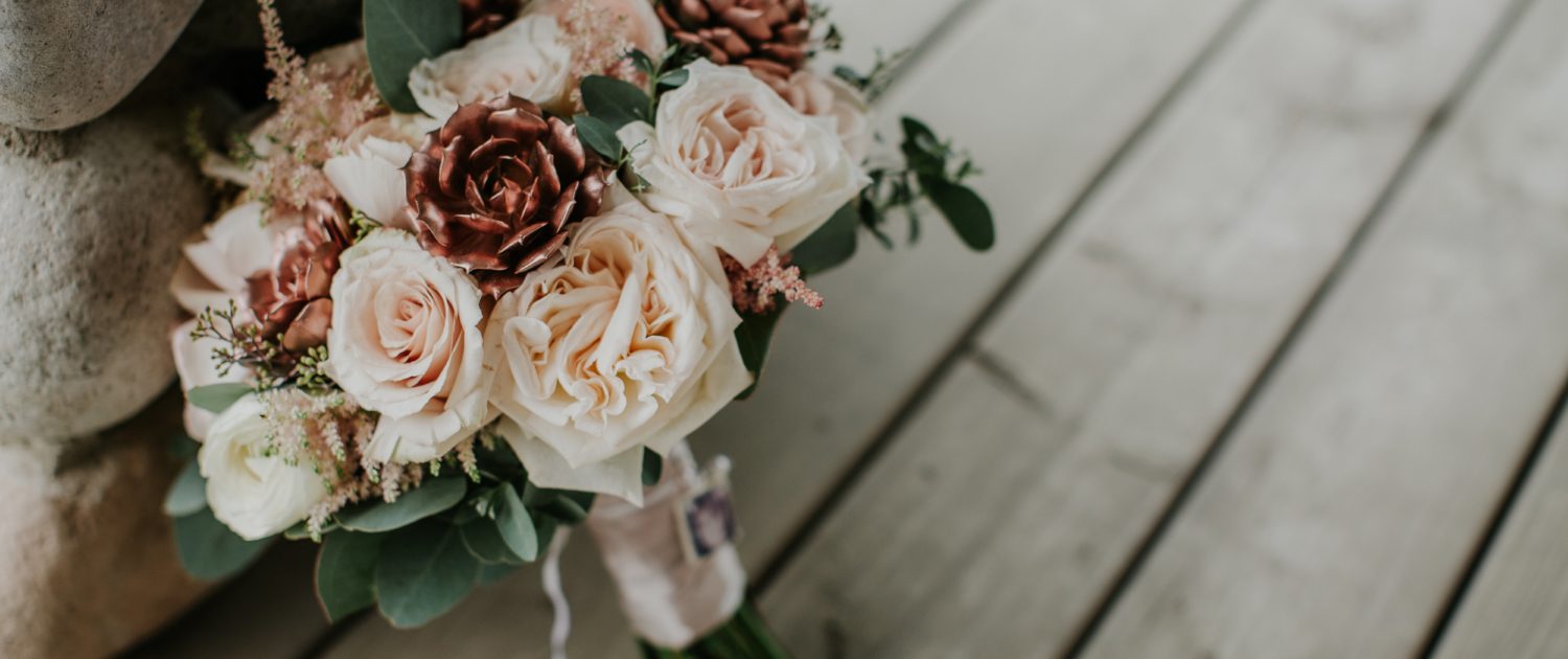 Close up detail shot of compact bridal bouquet made with white ohara garden roses and blush quicksand roses and astilbe and eucalyptus and rose gold succulents with brides photograph on the handle