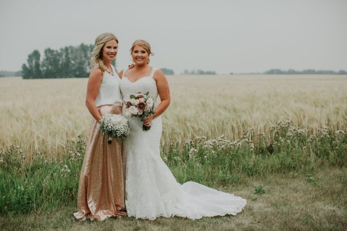 Bride with bridesmaid in a summer wheat field wearing a rose gold sequin bridesmaid dress holding a bouquet of babies breath and garden roses