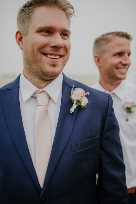 Groom in navy suit with blush tie and spray roses