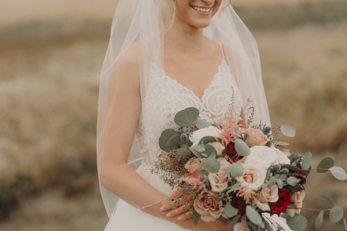 loose and romantic bridal bouquet with red roses and quicksand roses and white o'hara garden roses and pink astilbe and navy eryngium and mixed eucalyptus
