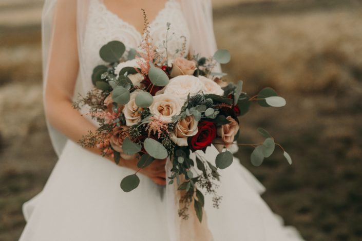 blush bridal bouquet with pops of red with red roses and quicksand roses and pink astilbe and blue eryngium and white o'hara garden roses and mixed eucalyptus in a loose and flowing style