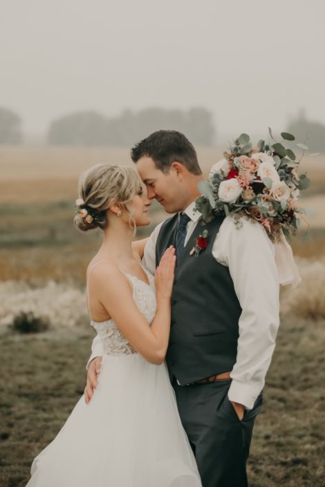 bride and groom portrait with hair flowers with pink spray roses and groom in grey suit with red spray rose boutonniere and bouquet with white o'hara garden roses and pink astilbe and quicksand roses and eucalyptus