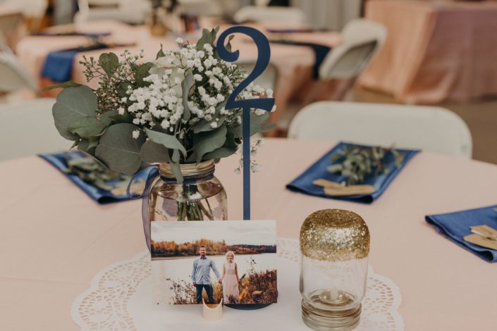 rustic table centerpiece with mason jar and blue ribbon and babies breath and eucalyptus and photograh of bride and groom and blue napkins