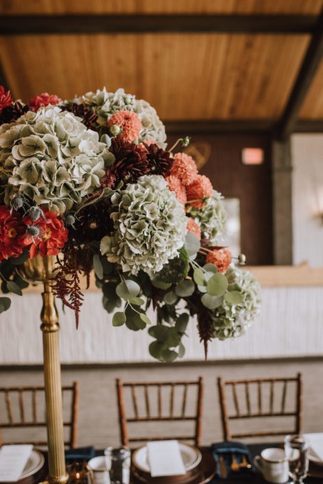 A stunning centerpiece designed atop a gold candleabra designed with hydrangea and burnt orange dahlia