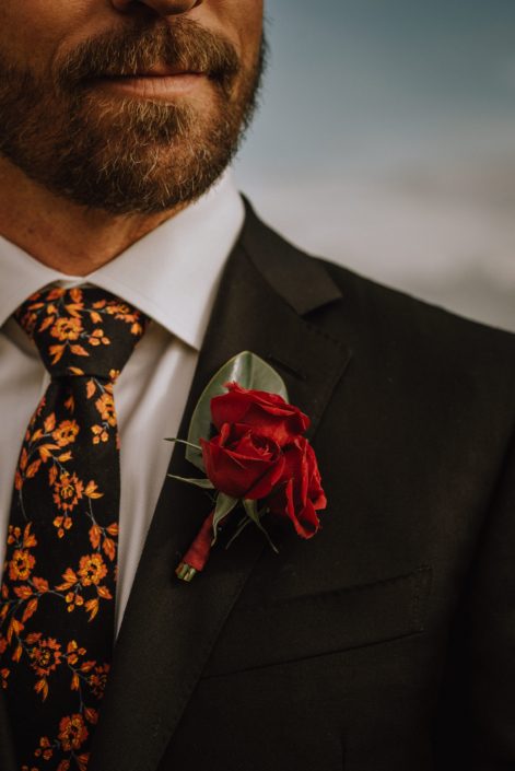 bearded groom wearing floral tie with red spray rose boutonniere